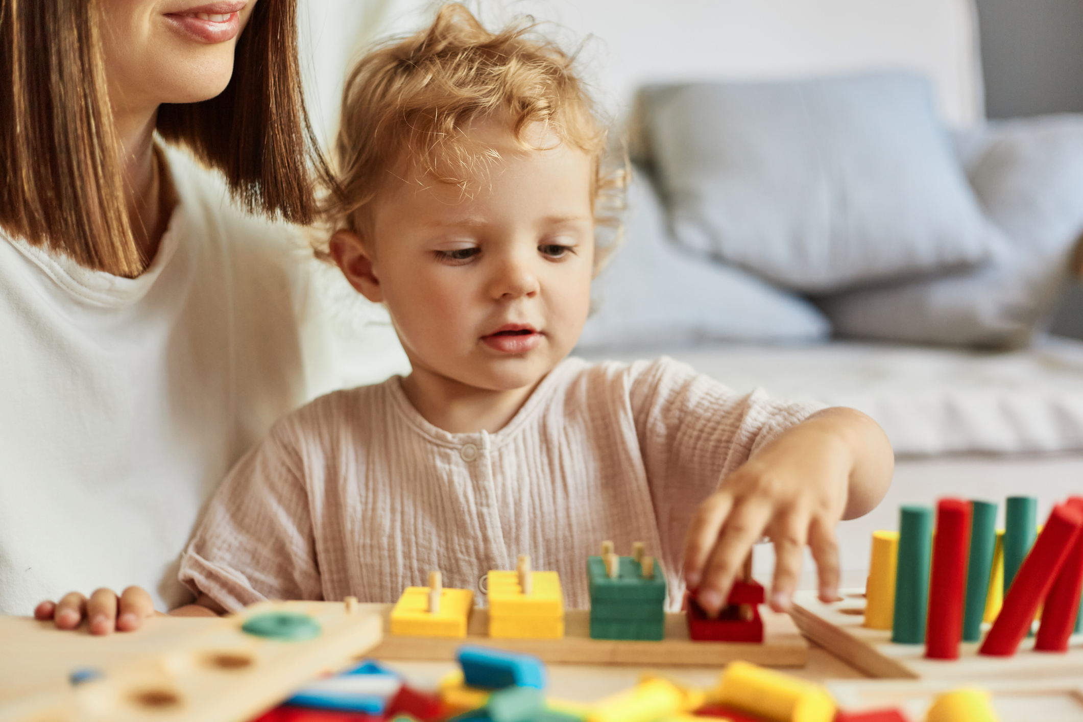 Cognitive development activities. Parent-child bonding experiences. Montessori learning tools. Preschooler's curious questions. Teacher or mother playing with baby with logical toys at home interior.